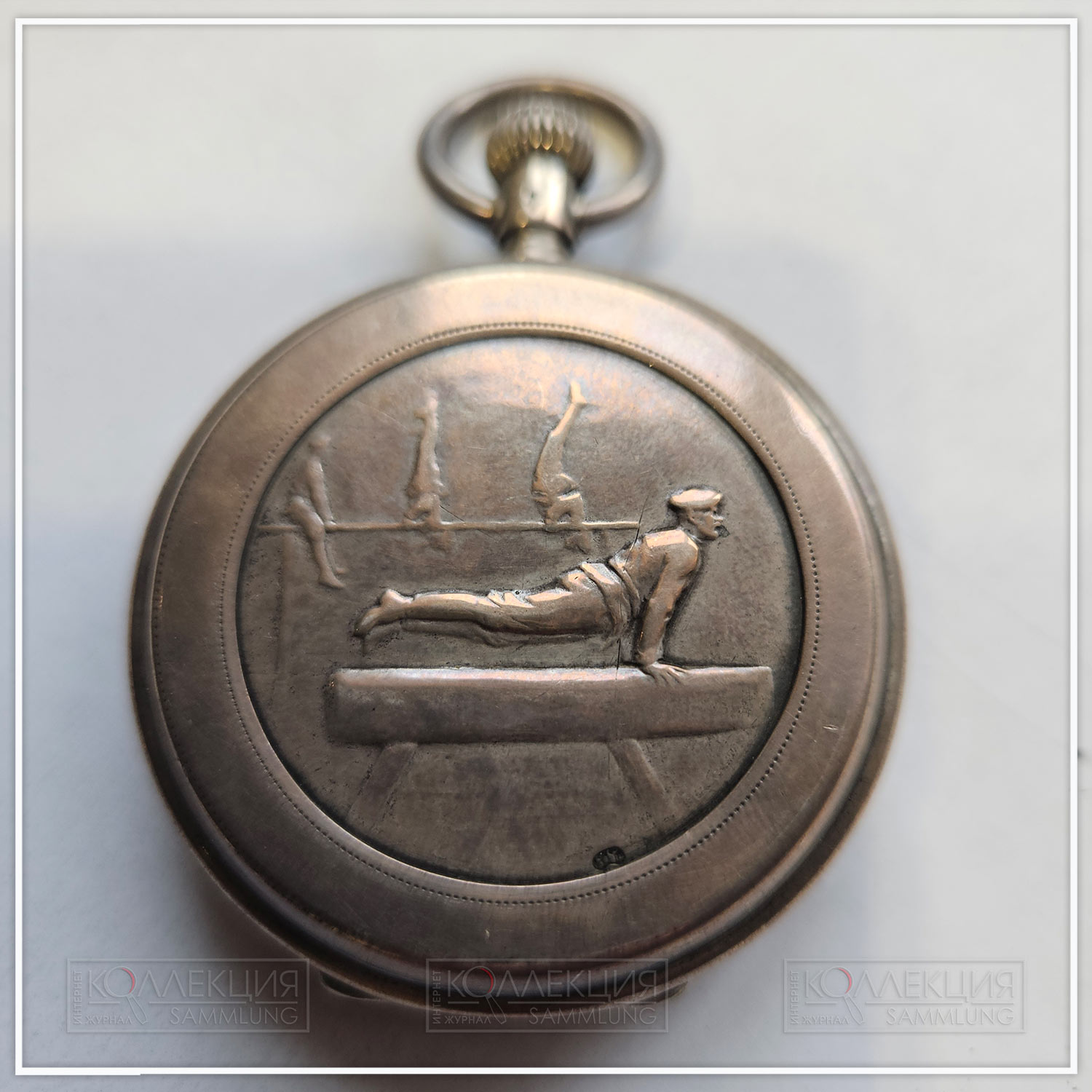 Серебряные закрытого типа (трёхкрышечные), Павел Буре. Тип корпуса «барабан» (drum), с гильоше, размер 50 мм, ремонтуар. На верхней крышке штампованное рельефное изображение солдат, занимающихся на коне и брусьях